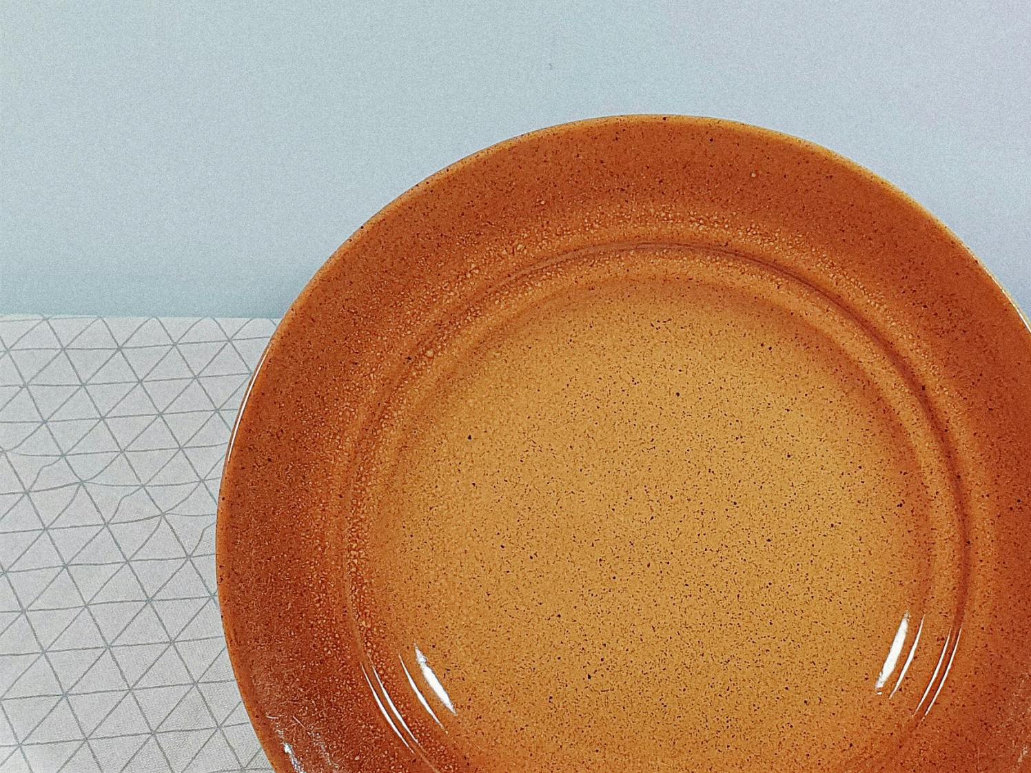 Orange plate on a white tablecloth on a wooden table
