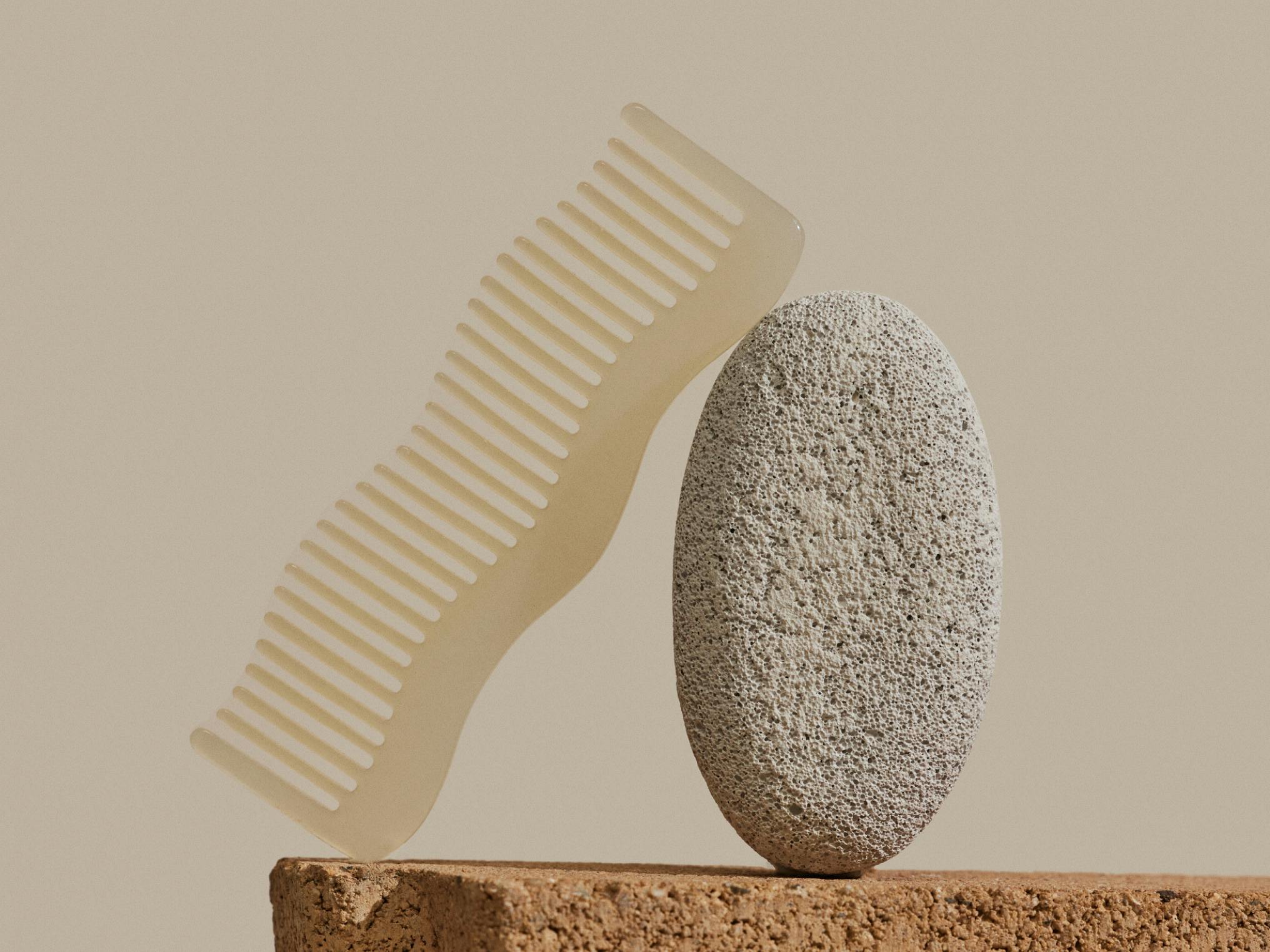 a beige hair comb propped up on a pumice stone, sitting on a tan stone surface