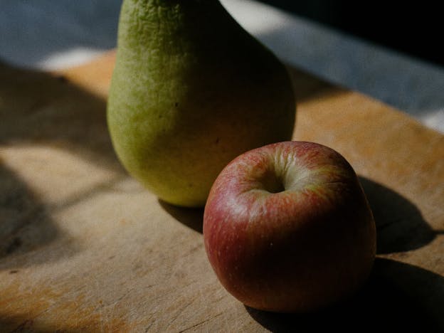 a pear and an apple on a wood cutting board