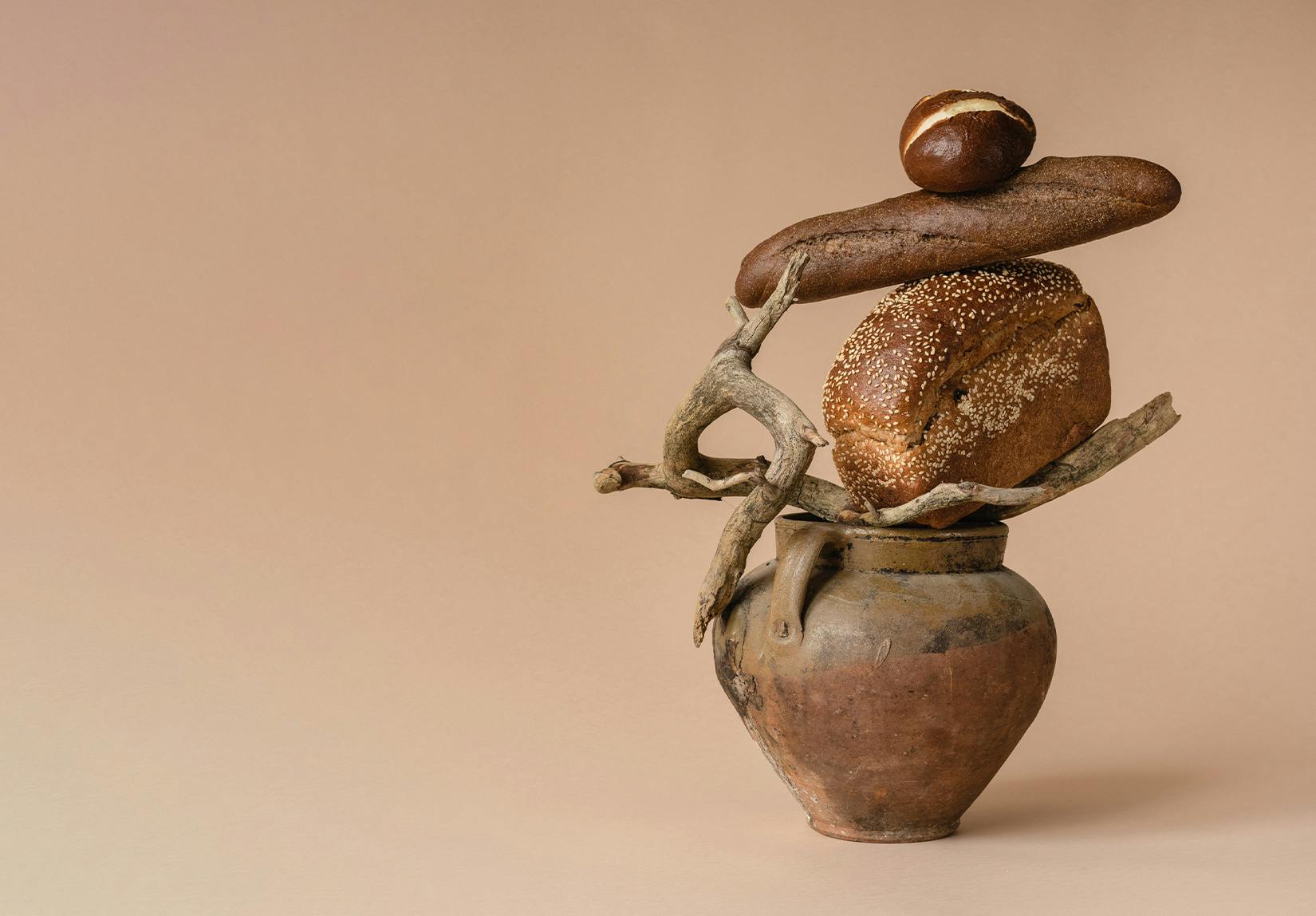 A brown vase topped with a branch and loaves of bread.
