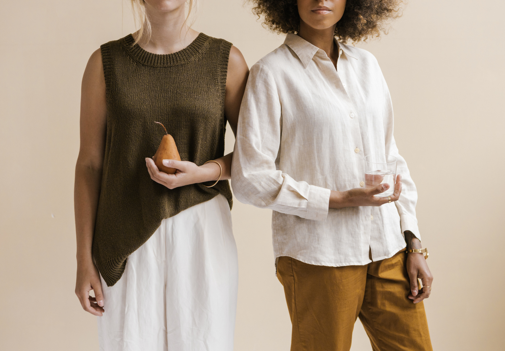 Two women standing side by side, one holding a pear and one holding a glass of water.